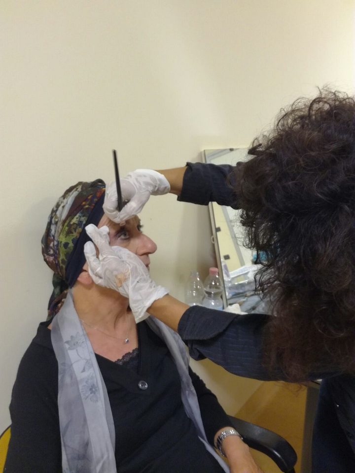 Annarita Minutaglio disegna a matita le sopracciglia di una donna in terapia oncologica, con il foulard in testa