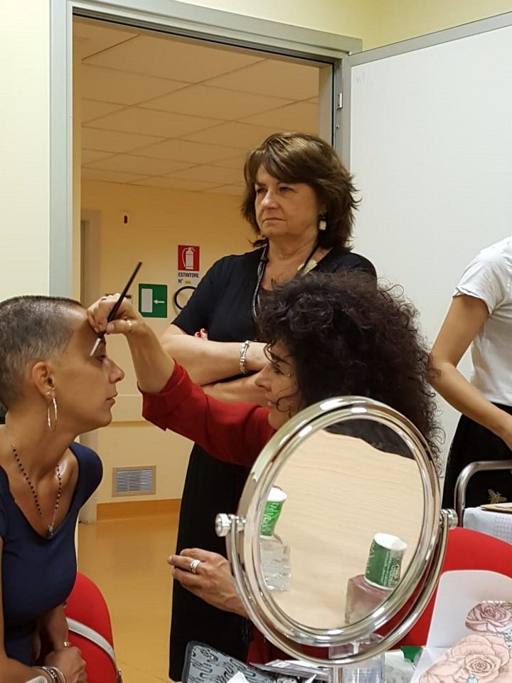 Annarita Minutaglio disegna a matita le sopracciglia di una donna in terapia oncologica, con uno specchio sul tavolo davanti a loro